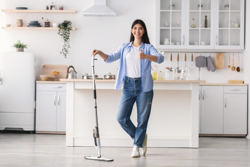 A woman standing in a white kitchen holding a map smiling and holding a thumbs up.