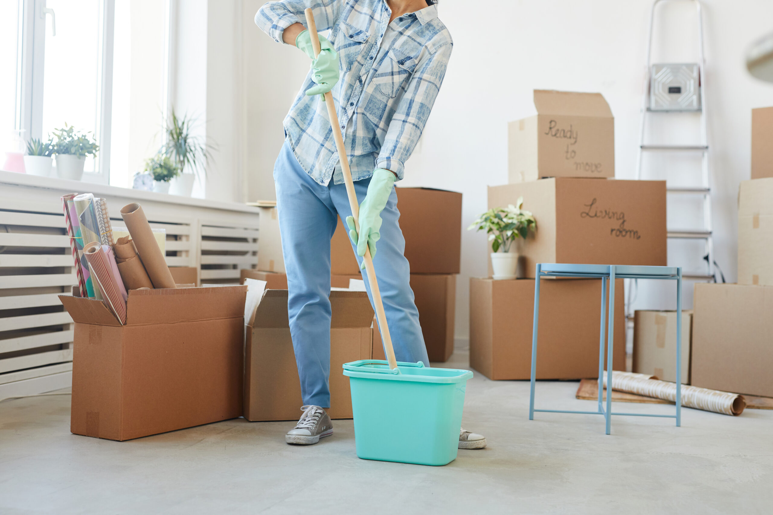 Cropped image of a person with a mop and mop bucket cleaning surrounded by cardboard moving boxes.